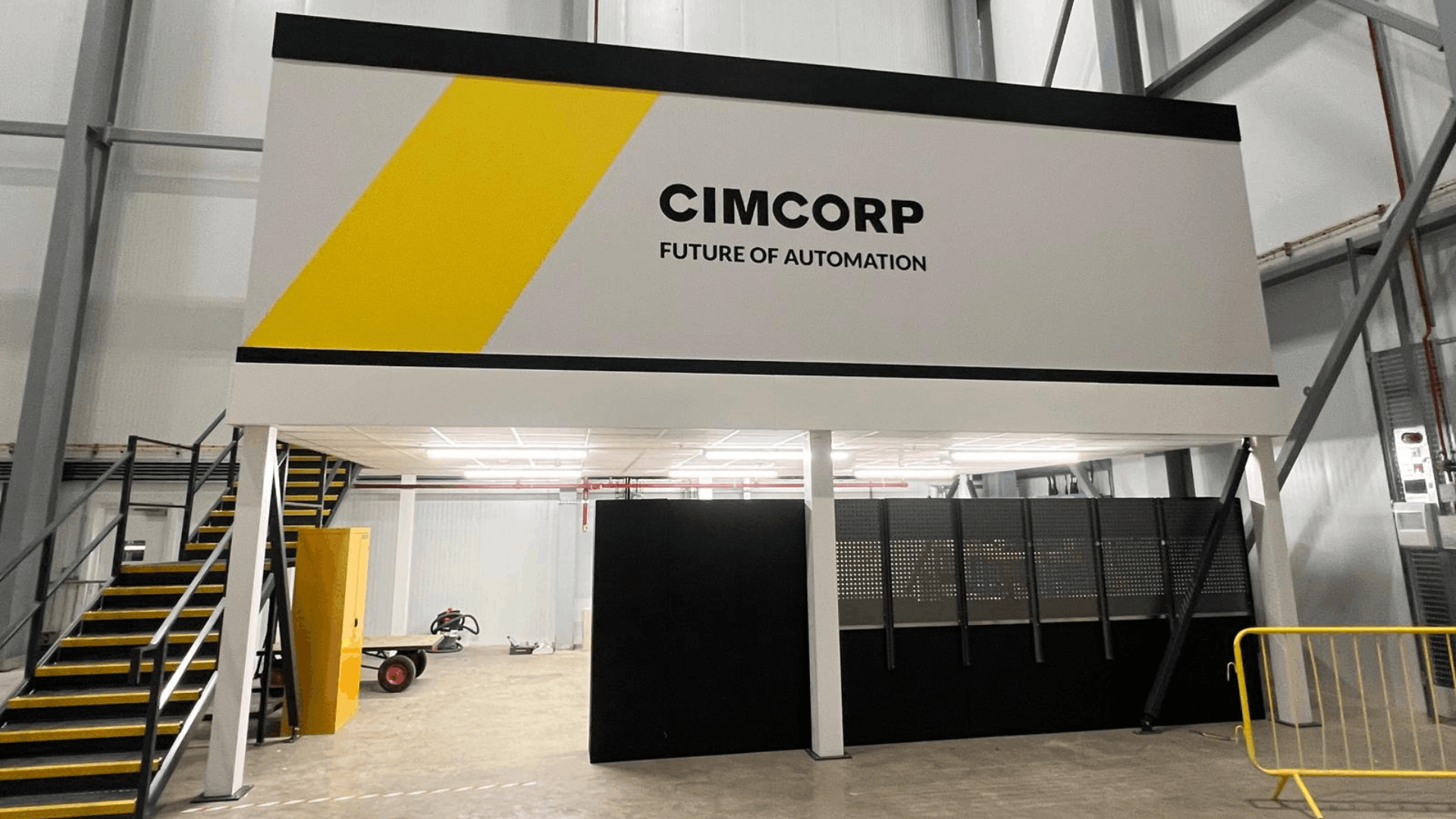 Front view of cimcorp mezzanine office structure with white fascia, black trim, yellow brand graphic and illuminated workspace beneath