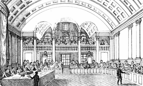 Ilustração em preto e branco do interior da Cadeia Velha, que abrigou a Assembleia Constituinte do Brasil em 1823. O desenho mostra uma sala grande com teto côncavo e várias colunas ao longo das paredes laterais. No centro da sala, há uma mesa em formato de 'U' ocupada por diversas pessoas com vestimentas masculinas, o que sugere serem todos homens. Alguns deles estão sentados, enquanto outros estão em pé, possivelmente discutindo ou apresentando algo. Nas galerias superiores, há mais pessoas assistindo ao que acontece na parte inferior. A ilustração apresenta um estilo detalhado, com atenção aos elementos arquitetônicos, como as colunas e os arcos.