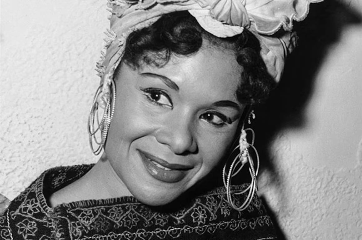 Fotografia em preto e branco da dançarina e coreógrafa afro-americana Katherine Dunham. Ela aparece de perfil, com os cabelos presos e adornos na cabeça, vestindo trajes típicos de dança. A imagem, registrada por Phyllis Twachtman e pertencente à Library of Congress, expressa a elegância e força de Dunham, referência na valorização das culturas afro-diaspóricas nas artes cênicas.