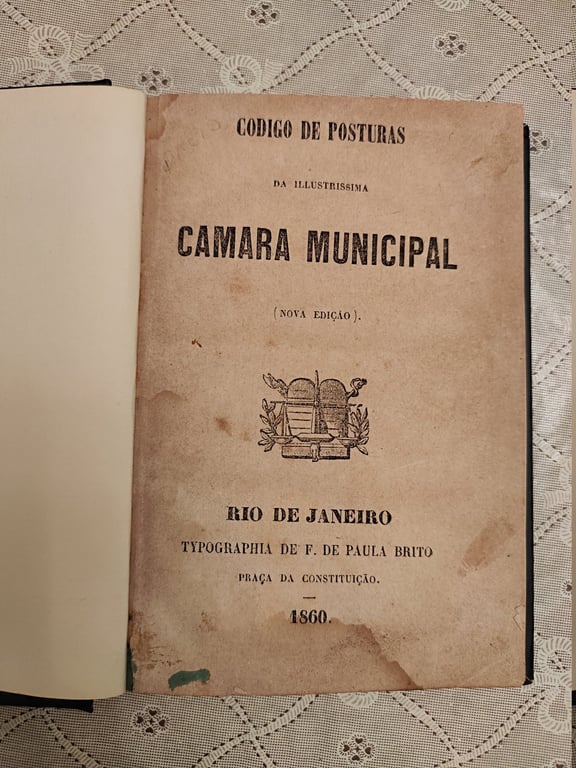 Contracapa do 'Código de Posturas' da Câmara Municipal do Rio de Janeiro, edição de 1860, impresso pela Tipografia de Francisco de Paula Brito. O livro tem páginas amareladas pelo tempo. Contém um brasão central com um feixe de ramos e um chapéu frígio, símbolo de liberdade. O título e as informações da edição estão dispostos em letras pretas, contrastando com o papel envelhecido. Francisco de Paula Brito (Rio de Janeiro, 2 de dezembro de 1809 – Rio de Janeiro, 5 de dezembro de 1861), mais conhecido como Paula Brito, foi um editor, jornalista, escritor, poeta, dramaturgo, tradutor e letrista negro e brasileiro. Atuou em diversas tipografias, tendo impresso o jornal O Mulato ou O Homem, título pioneiro da imprensa negra brasileira. Fundou a 'Sociedade Petalógica', da qual o jovem escritor Machado de Assis foi um membro destacado.
