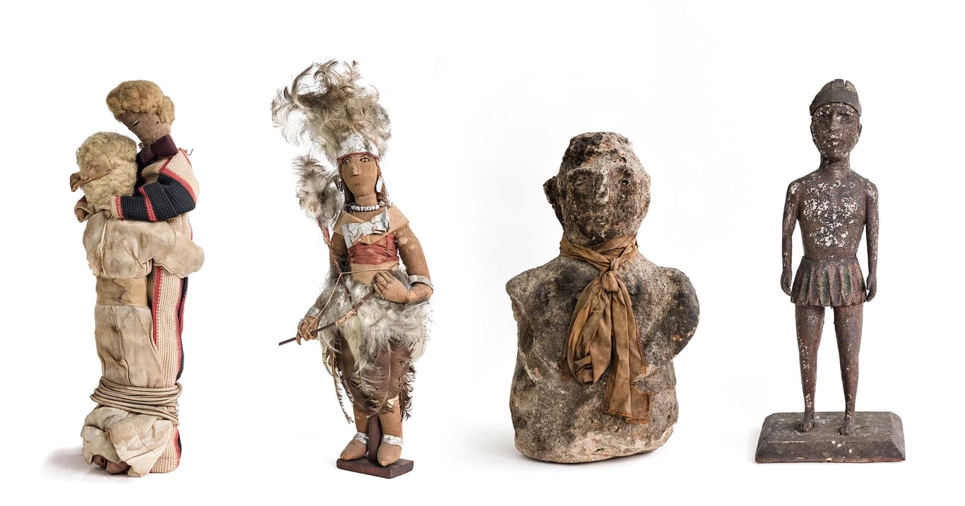 Fotografia colorida por Gui Christ, apresentando quatro objetos sacros de religiões afro-brasileiras. A imagem traz objetos sagrados que foram confiscados, revelando a persistente intolerância religiosa mesmo após o Decreto nº 119-A, de 7 de janeiro de 1890, que marcou o início do processo de laicização do Estado brasileiro ao oficializar a separação entre o Estado e a Igreja Católica. Nesta fotografia, da esquerda para a direita: o primeiro item é um par de bonecos de tecido em posição de abraço, com cabelos de lã e vestes em tons de bege, com detalhes vermelhos e pretos. O segundo é uma figura feminina com corpo de madeira, adornada com penas brancas, tecidos em tons terrosos e colares, segurando um arco e flecha. O terceiro é um busto de pedra, com rosto desgastado e um lenço marrom amarrado ao pescoço. O quarto objeto é uma escultura metálica de corpo inteiro, representando uma figura masculina com capacete e saia curta, sobre uma base retangular. Essas peças foram resgatadas em 2017 pelo movimento 'Liberte Nosso Sagrado'.