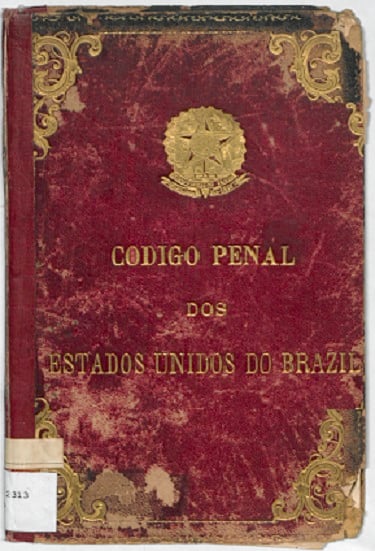Capa de um exemplar impresso do Código Penal dos Estados Unidos do Brazil, de 1890. O fundo é vermelho, bastante desgastado, com manchas, arranhões e bordas danificadas pelo tempo. No topo da capa está o brasão da República do Brasil em dourado. Abaixo, o título aparece em letras douradas e serifadas. Ornamentações douradas decoram os cantos superior direito e inferior esquerdo. O documento representa a institucionalização da justiça criminal no início da República, com foco em consolidar uma ordem legal moderna, influenciada pelo positivismo e pela ideia de controle social por meio da punição.