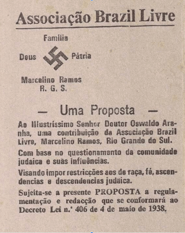 Imagem do acervo do Centro de Memória do Museu Judaico de São Paulo, que mostra um panfleto da Associação Brazil Livre pertencente ao Marcelino Ramos, do Rio Grande do Sul, com discurso antissemita. No topo, o título 'Associação Brazil Livre' aparece centralizado, seguido por um símbolo nazista (suástica) entre as palavras 'Deus' e 'Pátria', além de 'Família' escrita acima da cruz suástica. Abaixo, o texto apresenta uma proposta enviada ao então Ministro da Justiça Oswaldo Aranha, defendendo restrições a pessoas de 'raça, fé, ascendências e descendências judaicas', sob alegação de questionar a 'comunidade judaica e suas influências'. O documento afirma que a proposta se adequaria ao Decreto-Lei nº 406 de 4 de maio de 1938, que estabeleceu regras rigorosas para a entrada de pessoas estrangeiras no Brasil. A peça escancara a influência de ideias nazifascistas no Brasil dos anos 1930, sustentadas por segmentos da sociedade civil e apoiadas por legislações com forte conteúdo eugênico, racista e xenófobo.
