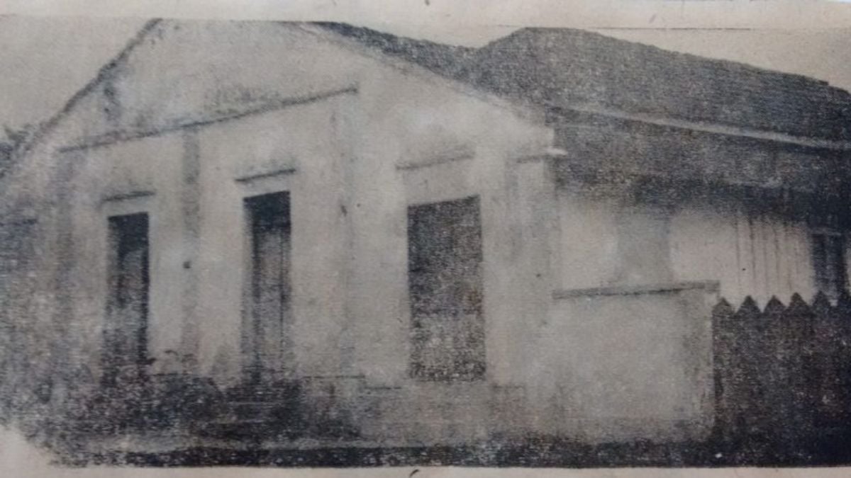 Fotografia em preto e branco de uma construção simples, térrea, com telhado de duas águas e paredes claras. A fachada exibe três portas retangulares alinhadas, com molduras discretas. O tempo e a qualidade da imagem conferem ao registro um aspecto envelhecido e granulado. Trata-se da sede do Kênia Clube, em Joinville (SC), importante sociedade recreativa negra fundada em 1950, que se tornou um espaço de encontro, cultura e resistência para a comunidade afrodescendente na cidade.