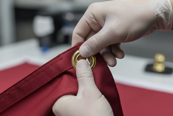 Step 5 - Quality check: Testing installed flag grommet by tugging to verify it doesn't move, spin, or feel loose, ensuring proper installation before custom flag deployment in outdoor conditions