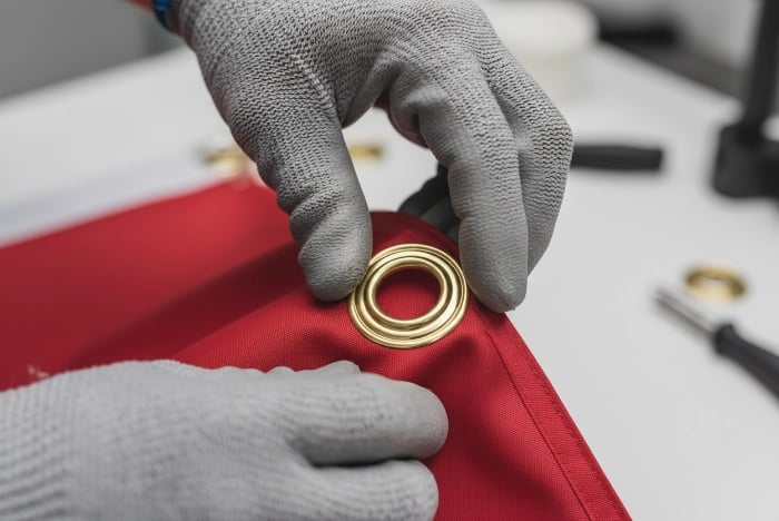 Step 2 - Insert grommet base: Pushing brass or stainless steel grommet base through punched hole from front side of flag fabric, ensuring flush contact without wiggle room for secure custom flag installation