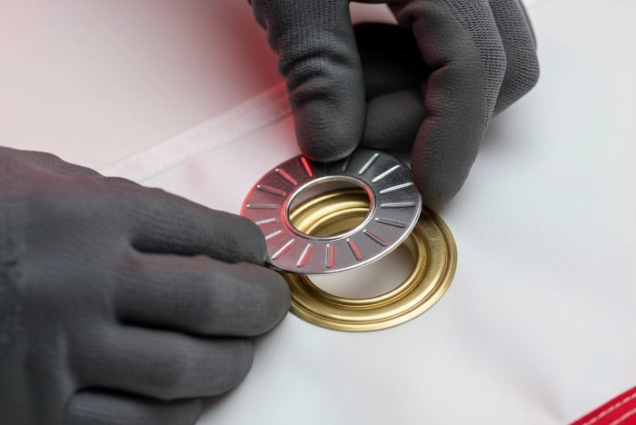 Step 3 - Add washer ring: Placing metal washer ring on back side of flag fabric over grommet base to distribute load evenly and prevent pull-through during high wind conditions on outdoor custom flags