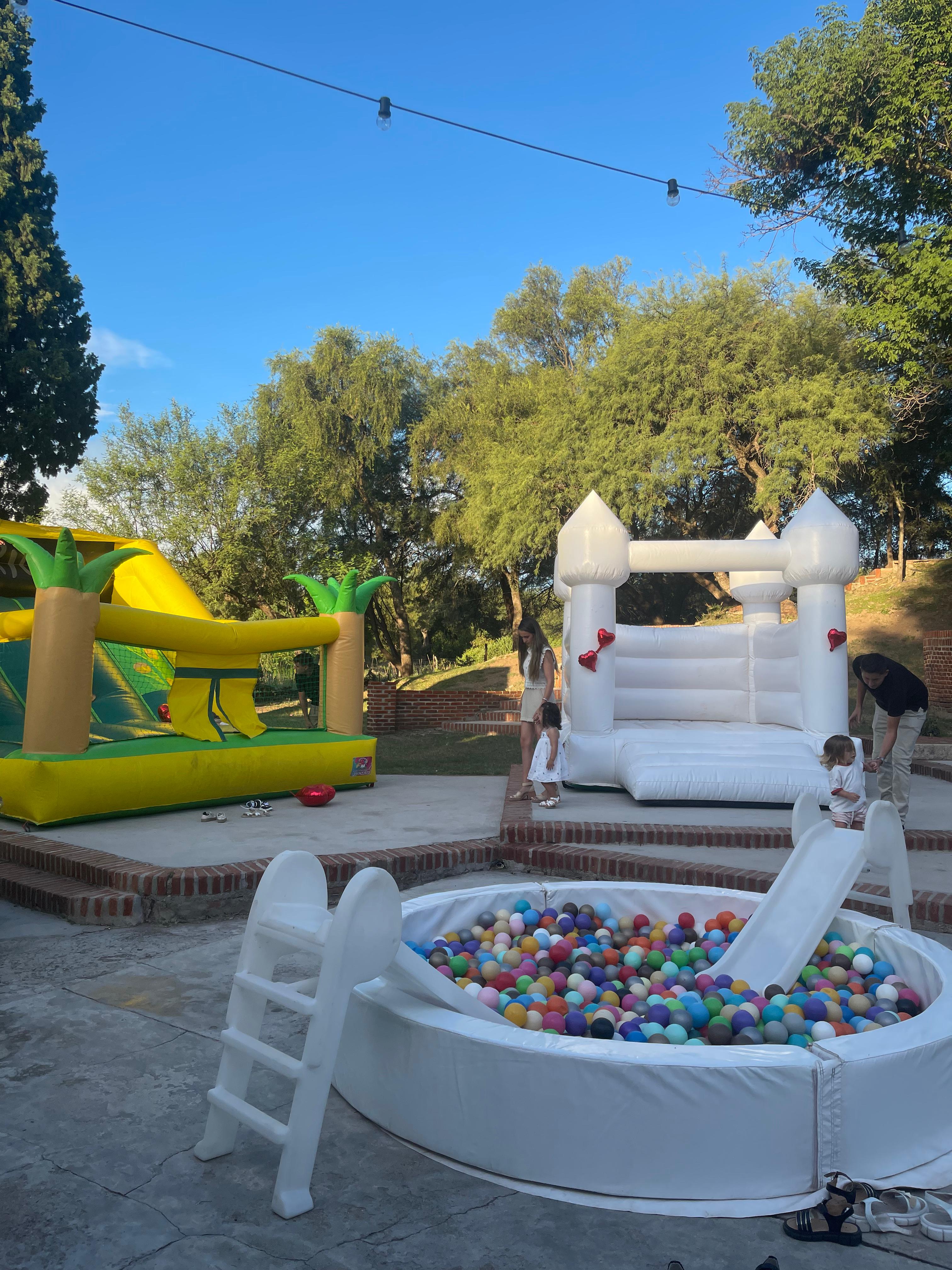 Zona de inflables al aire libre con castillo, pelotero y tobogán entre árboles