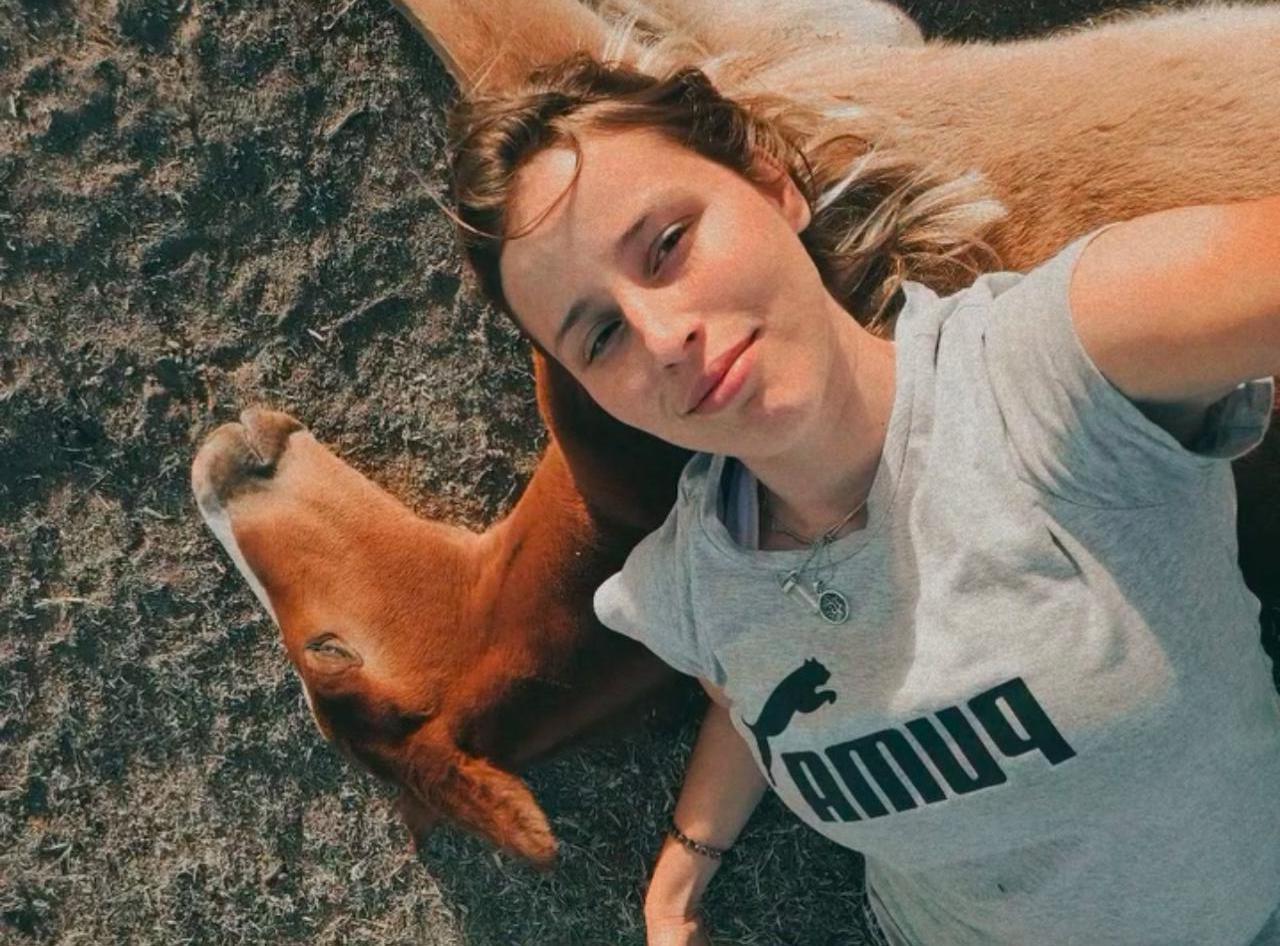 Angie, fundadora de África, recostada en el pasto junto a un potrillo
