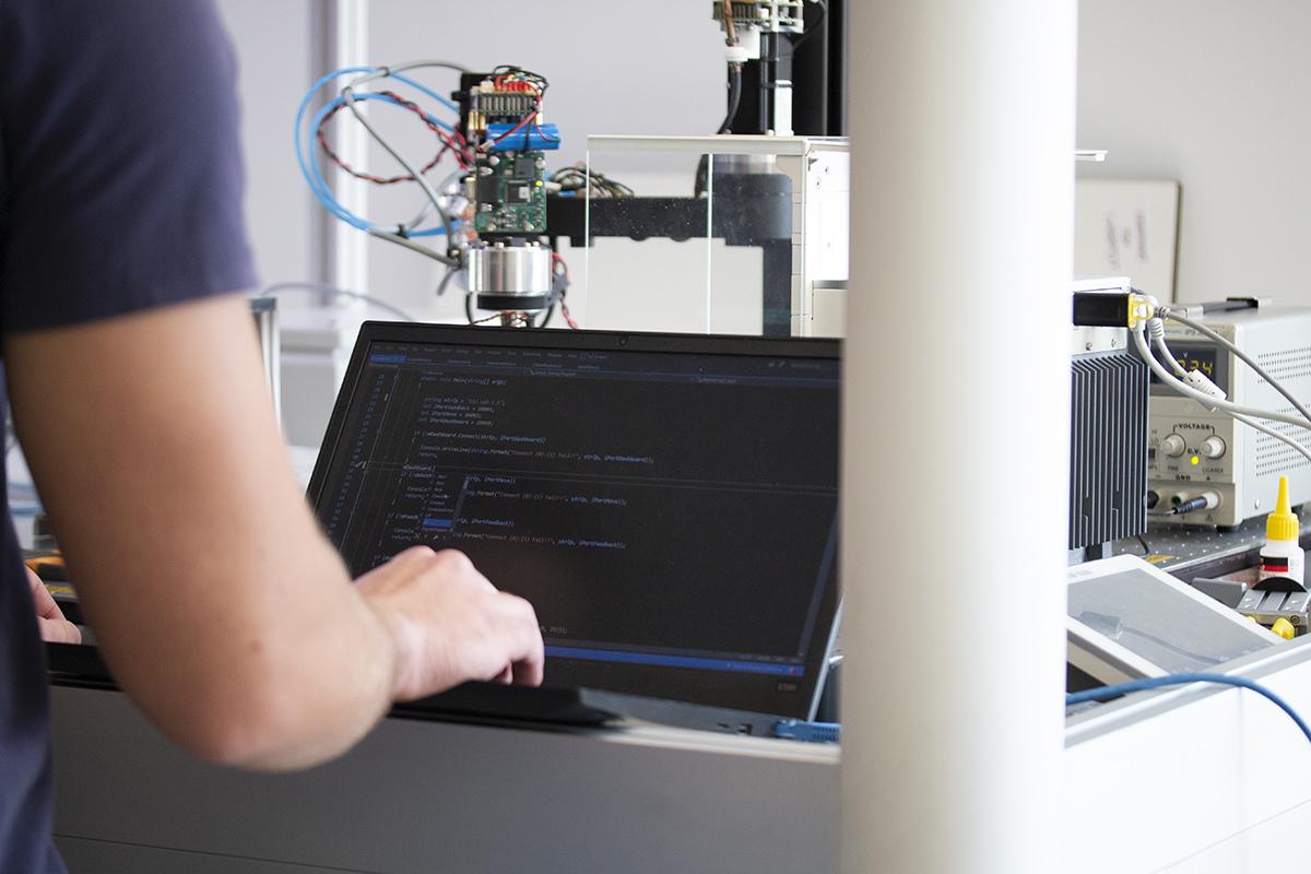 Person typing on laptop with robot system in background