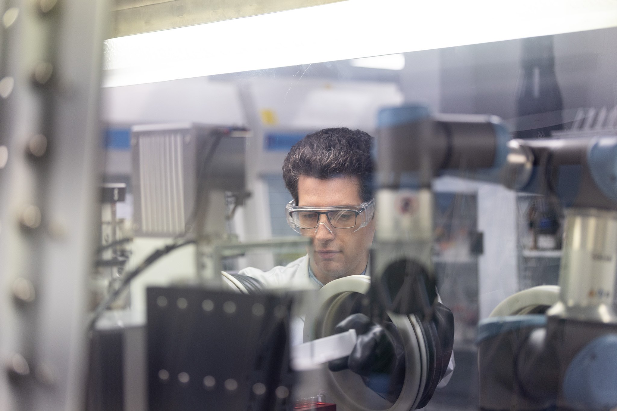 A man wearing safety specs using a glovebox in a laboratory