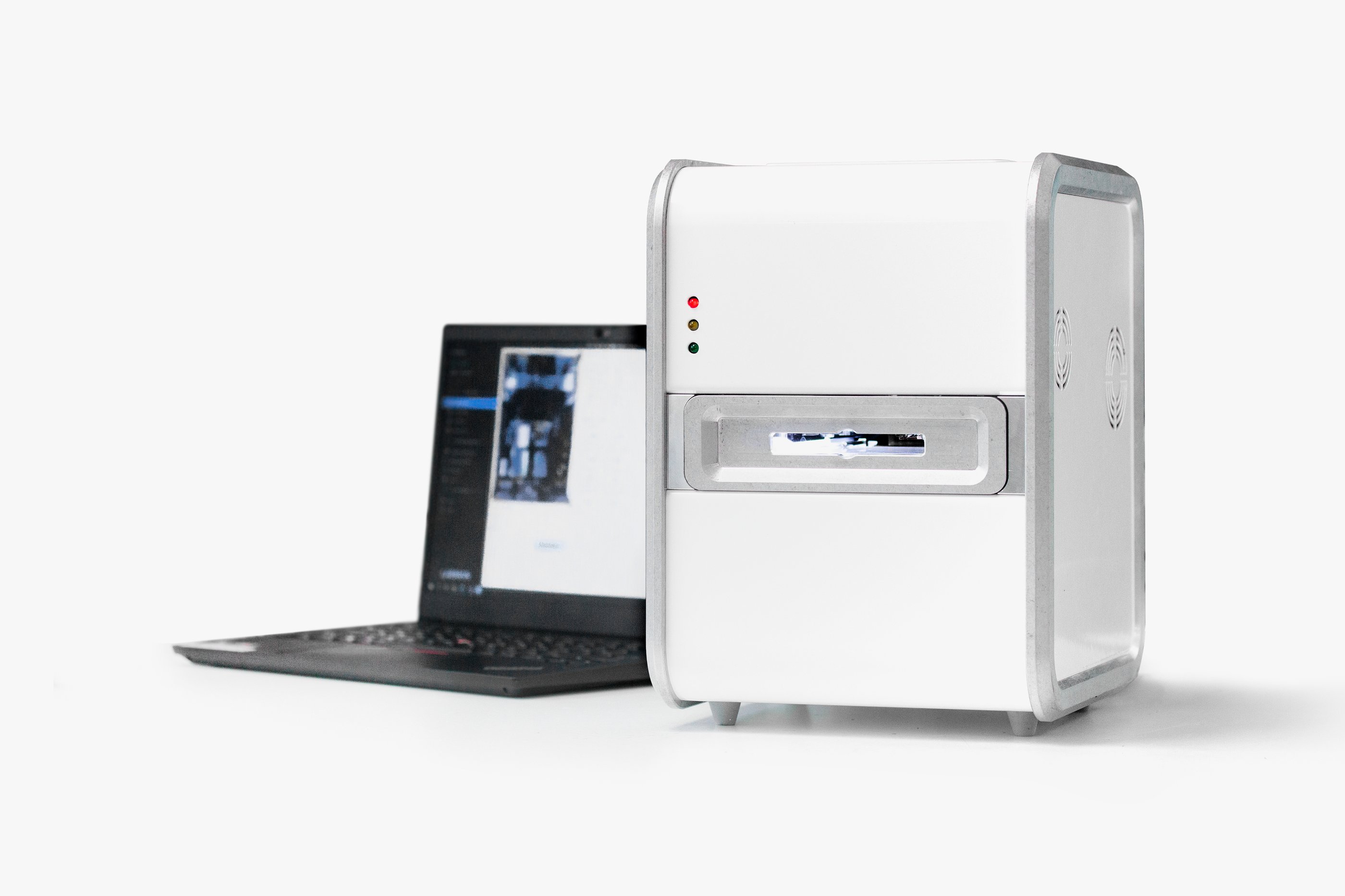 A white cuboid medical device with a grey laptop next to it in a white room
