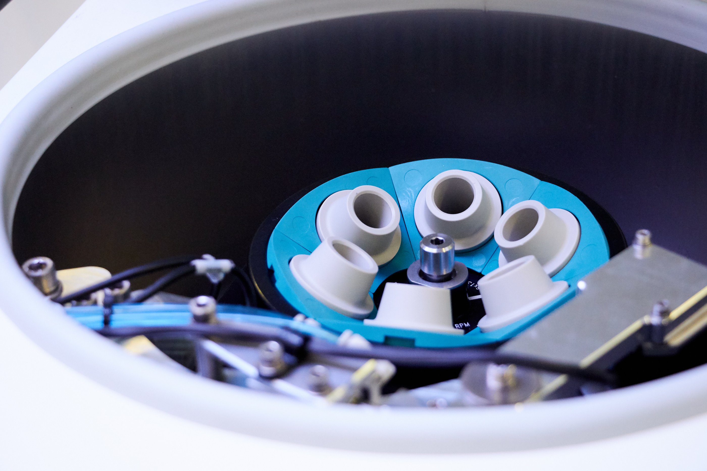 A close up of blue circular piece of lab equipment with white holes and wires coming out of it