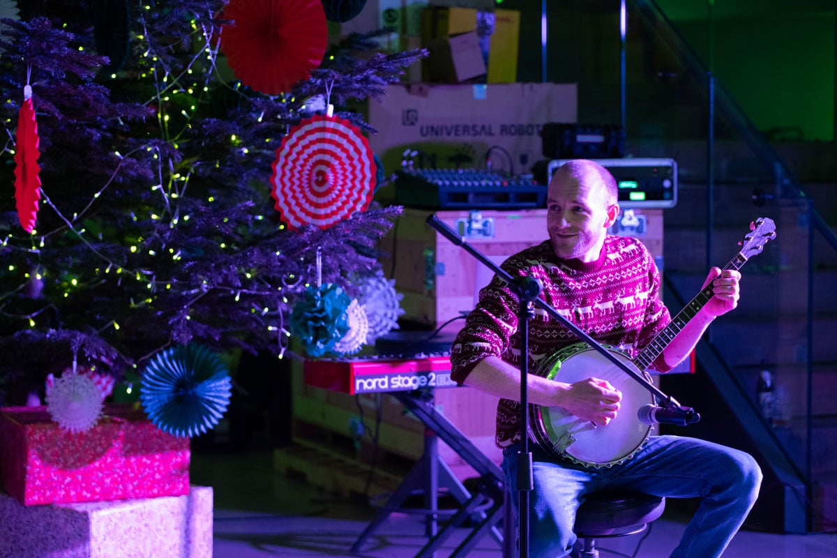 man sits in front of christmas tree playing banjo