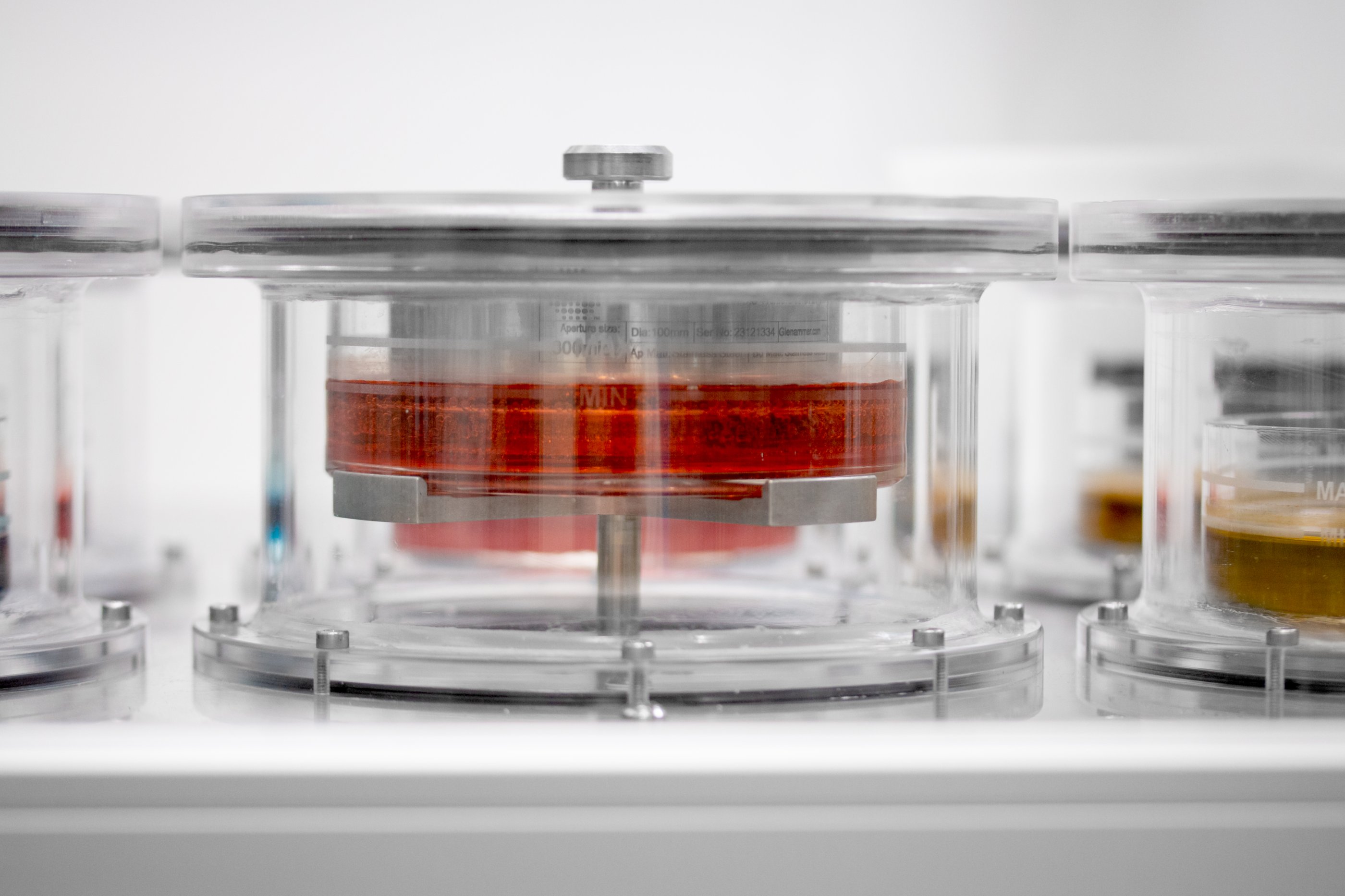 Dipping vessel containing a clear pot filled with a red liquid solution. The steel basket containing porous pellets is submerged in the liquid