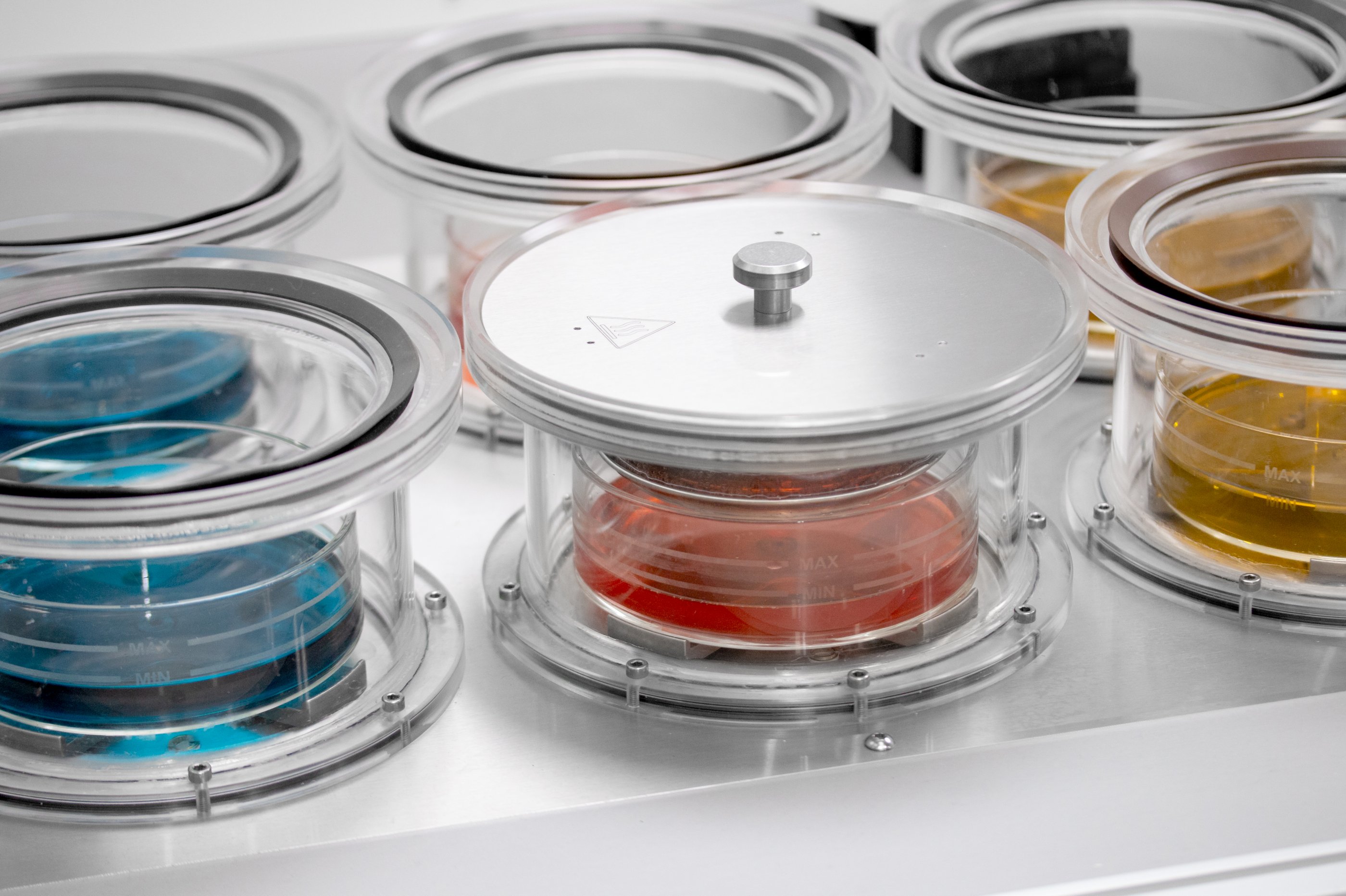 Dipping vessel containing a clear pot filled with a red liquid solution. The steel basket containing porous pellets is submerged in the liquid