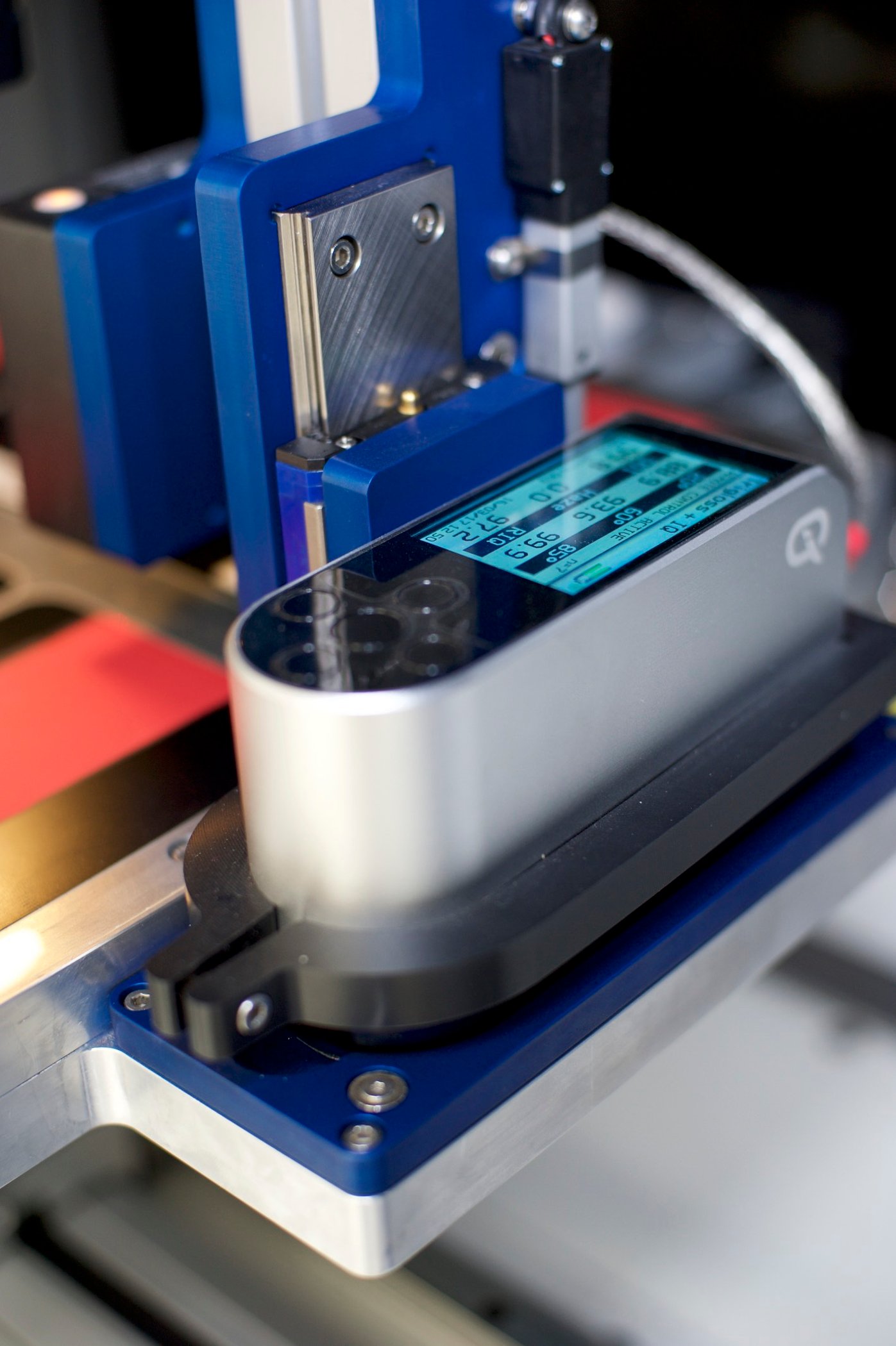 A paint analysis gloss meter attached to a metal frame inside an automated lab robot