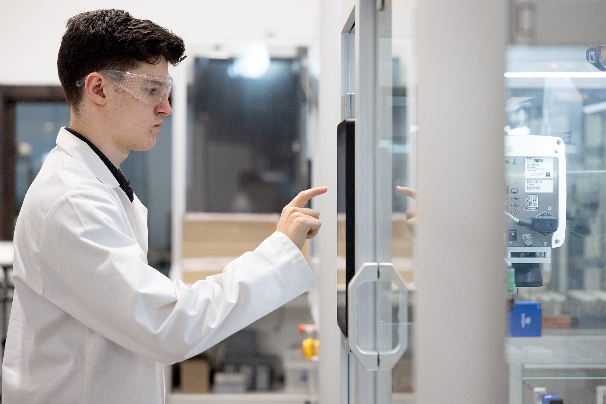 A male lab technician wearing safety specs using a screen on a robotic system