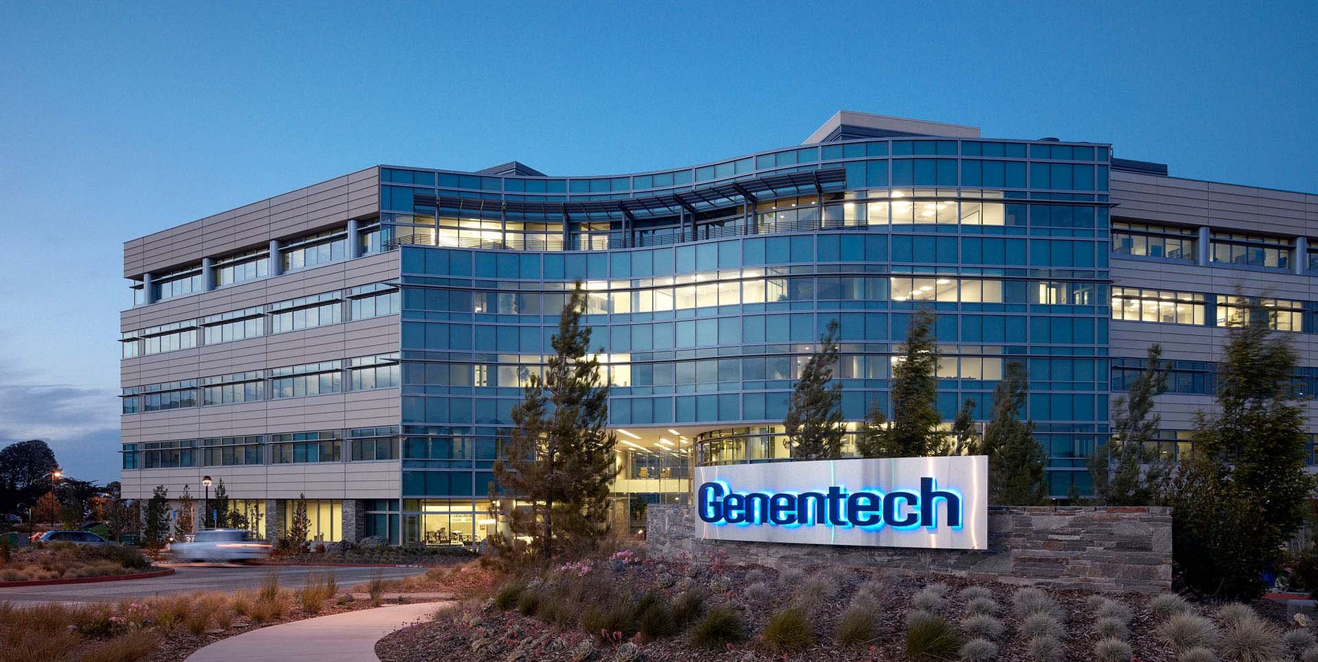 Modern building at dusk with lights on in some offices and Genetech sign in front