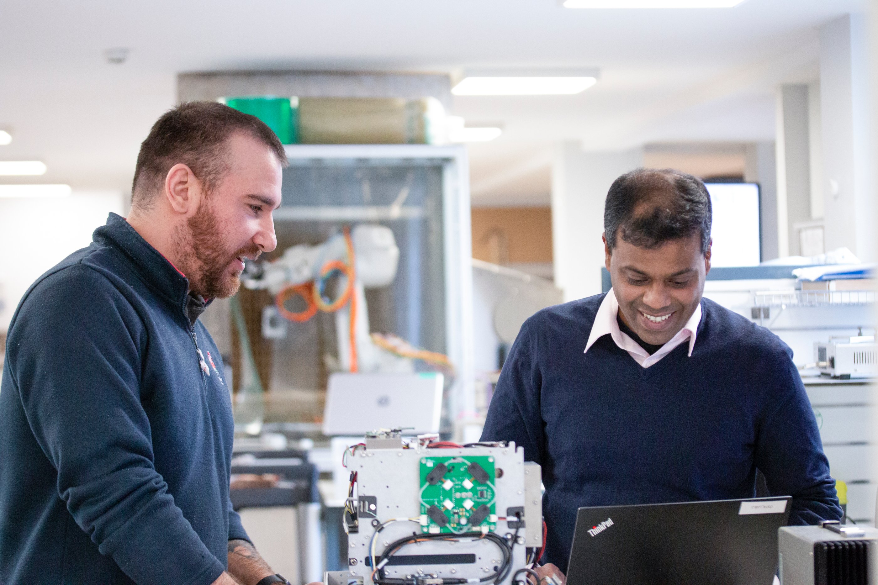 2 men looking down, smiling, at a laptop in a laboratory setting