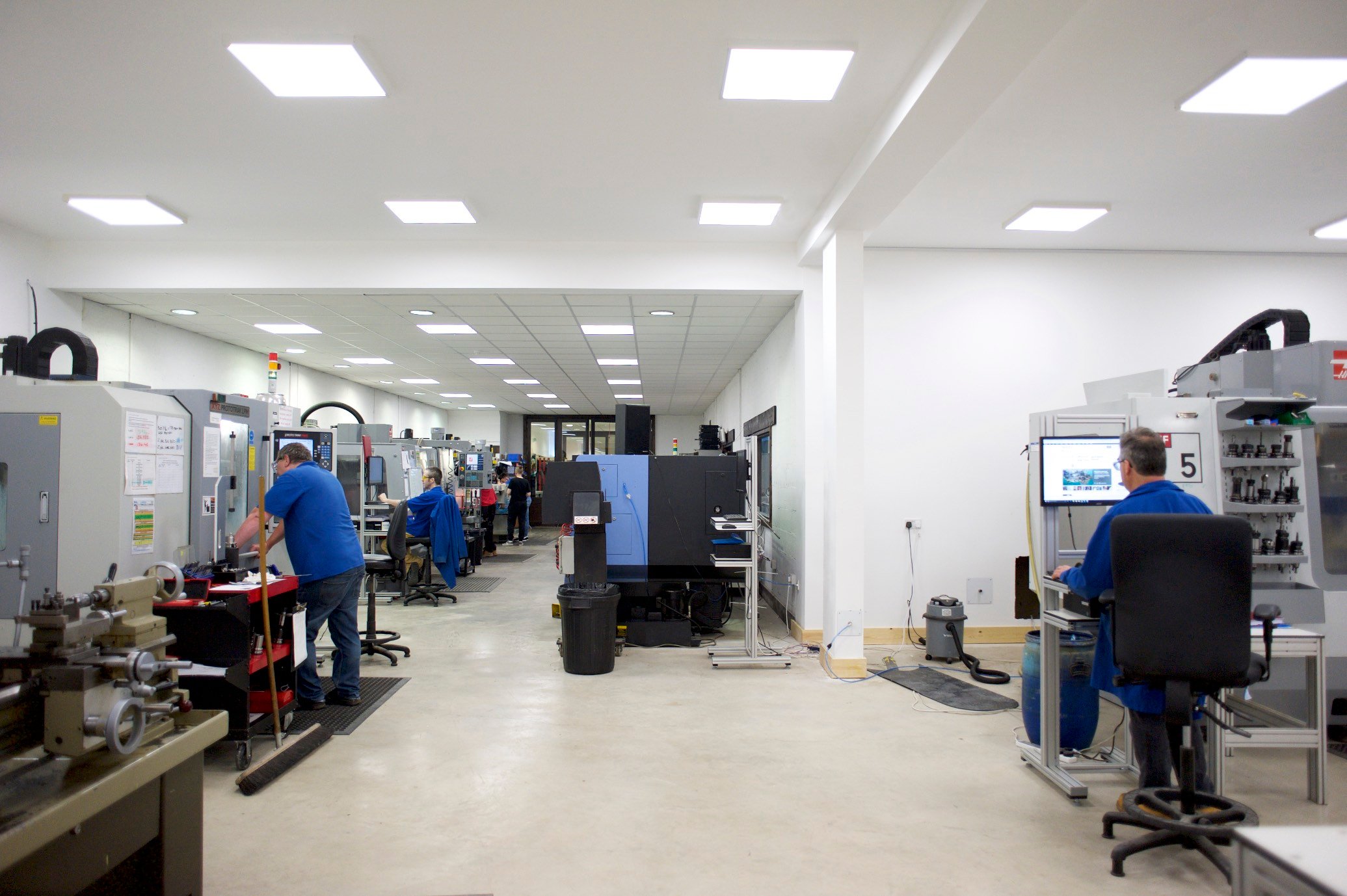 A white lab with robotic systems and workflows being tinkered with by people in blue polos