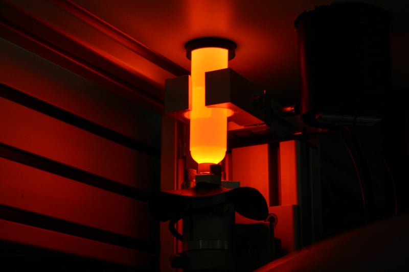 An enclosed, lit up orange test tube being held by a robotic gripper