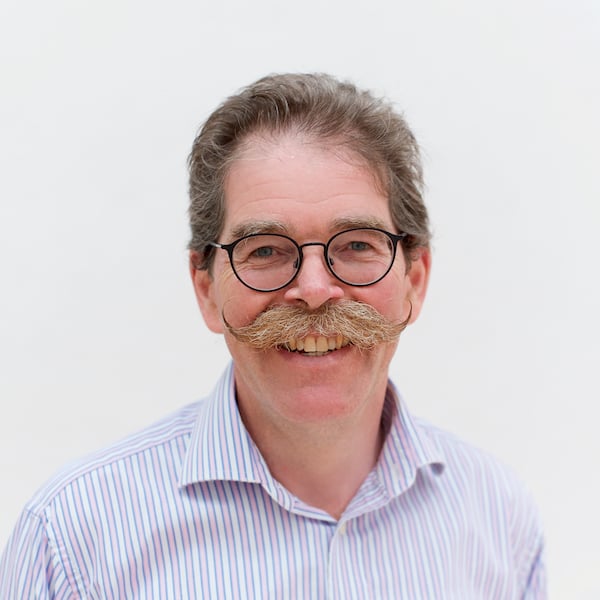 A headshot of a man with glasses and a moustache on a white background