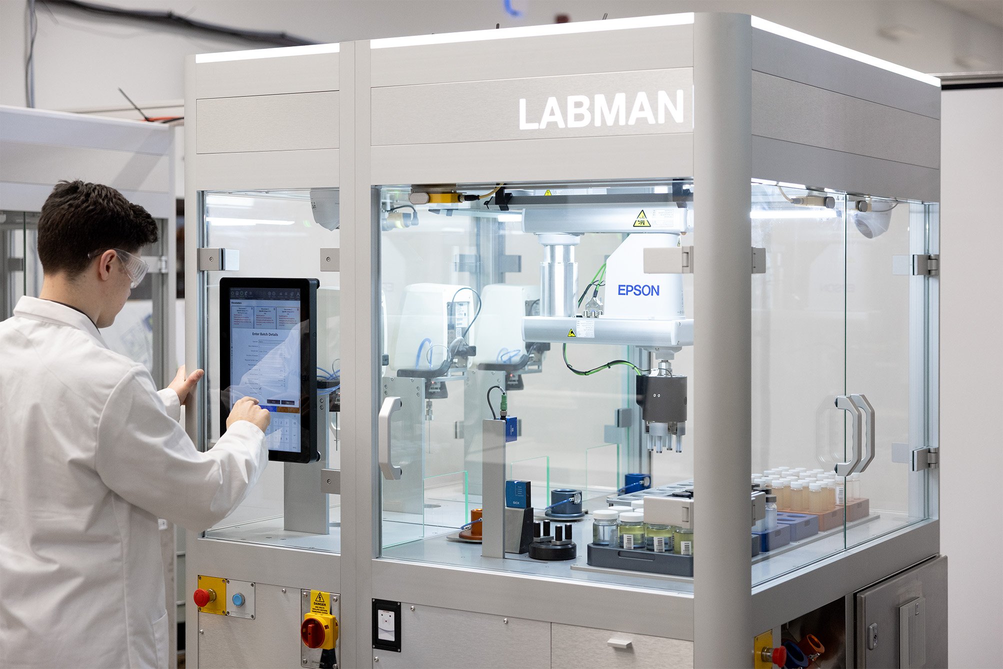 A male lab technician wearing safety specs using a screen on a robotic system