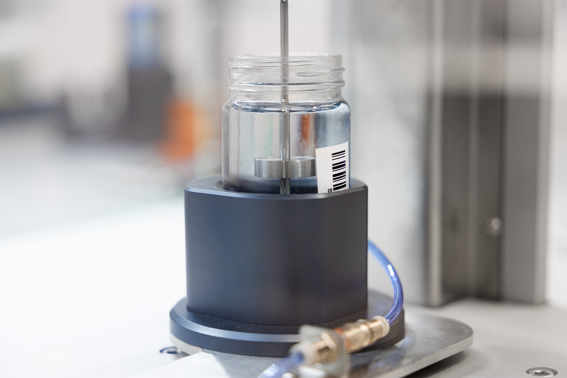 A geometry used for taking viscometry measurements being lowered into a jar of liquid