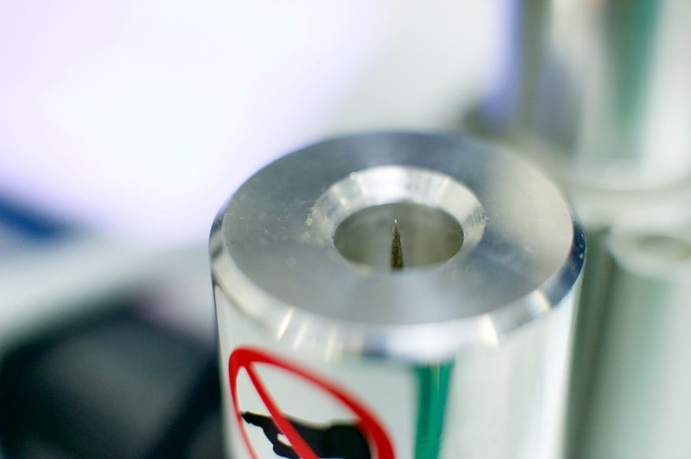 A needle coming out of a metal tube with a blurry silver and white background 