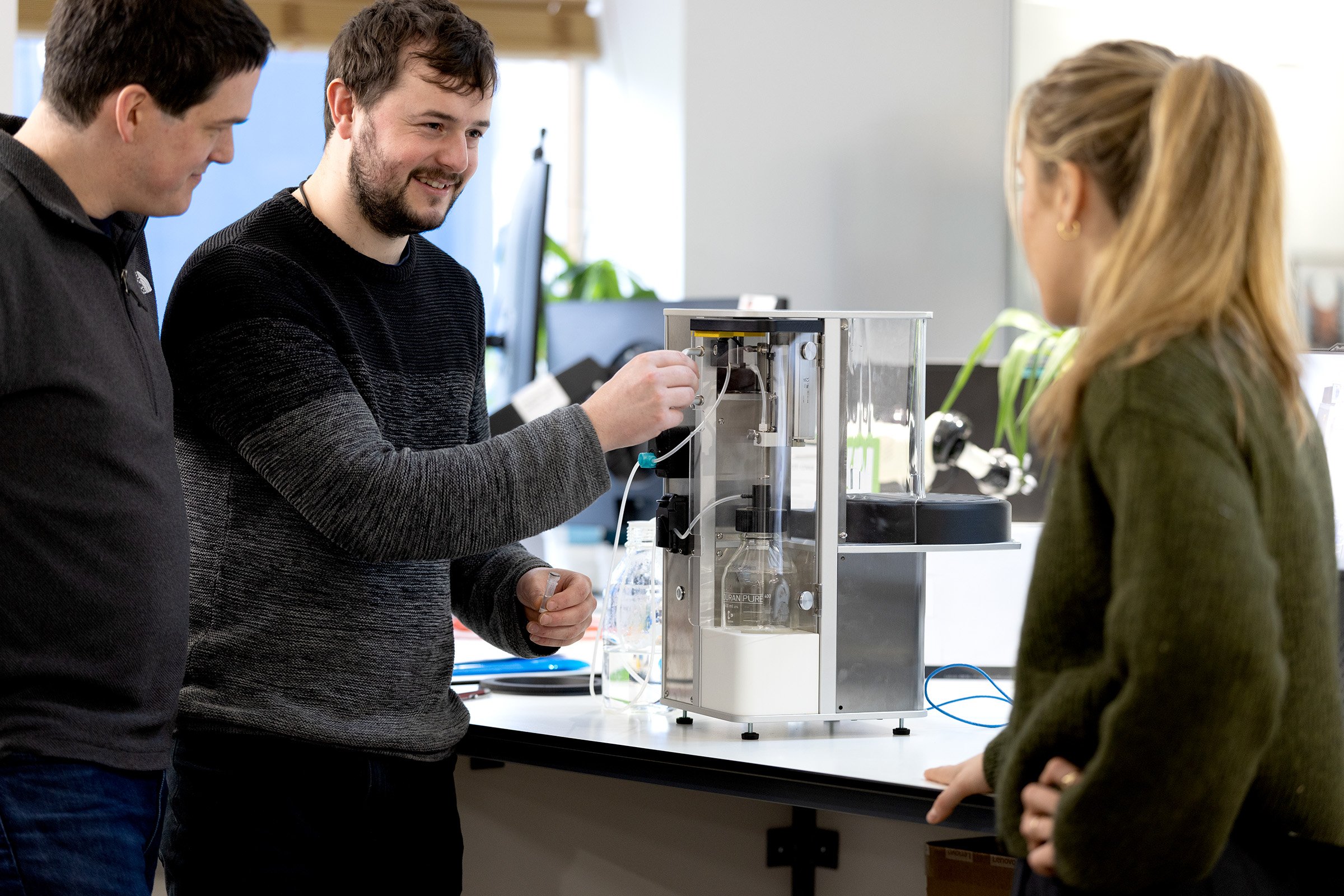 A group of smiling bioprocess engineers looking at a sampling device