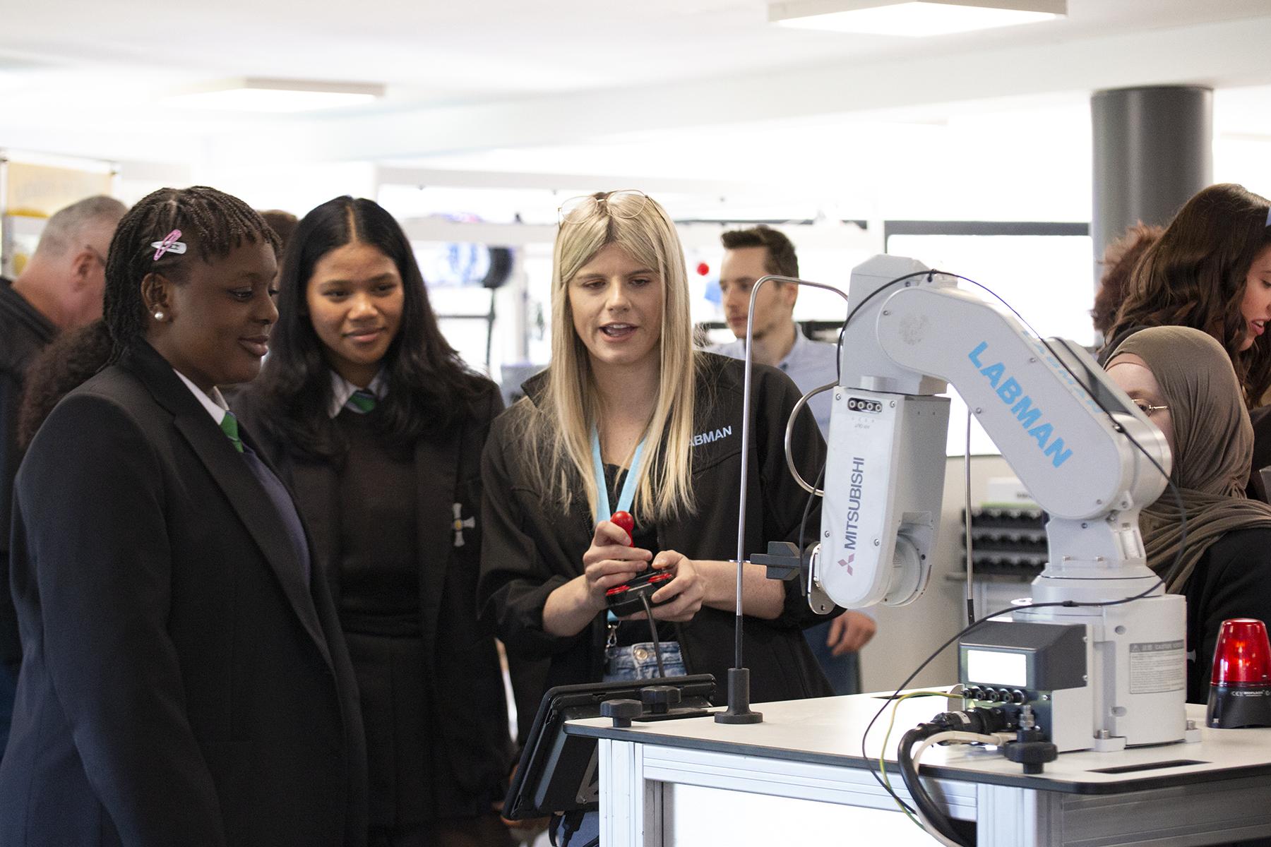 Female school students stand with Labman team member discovering a robot arm