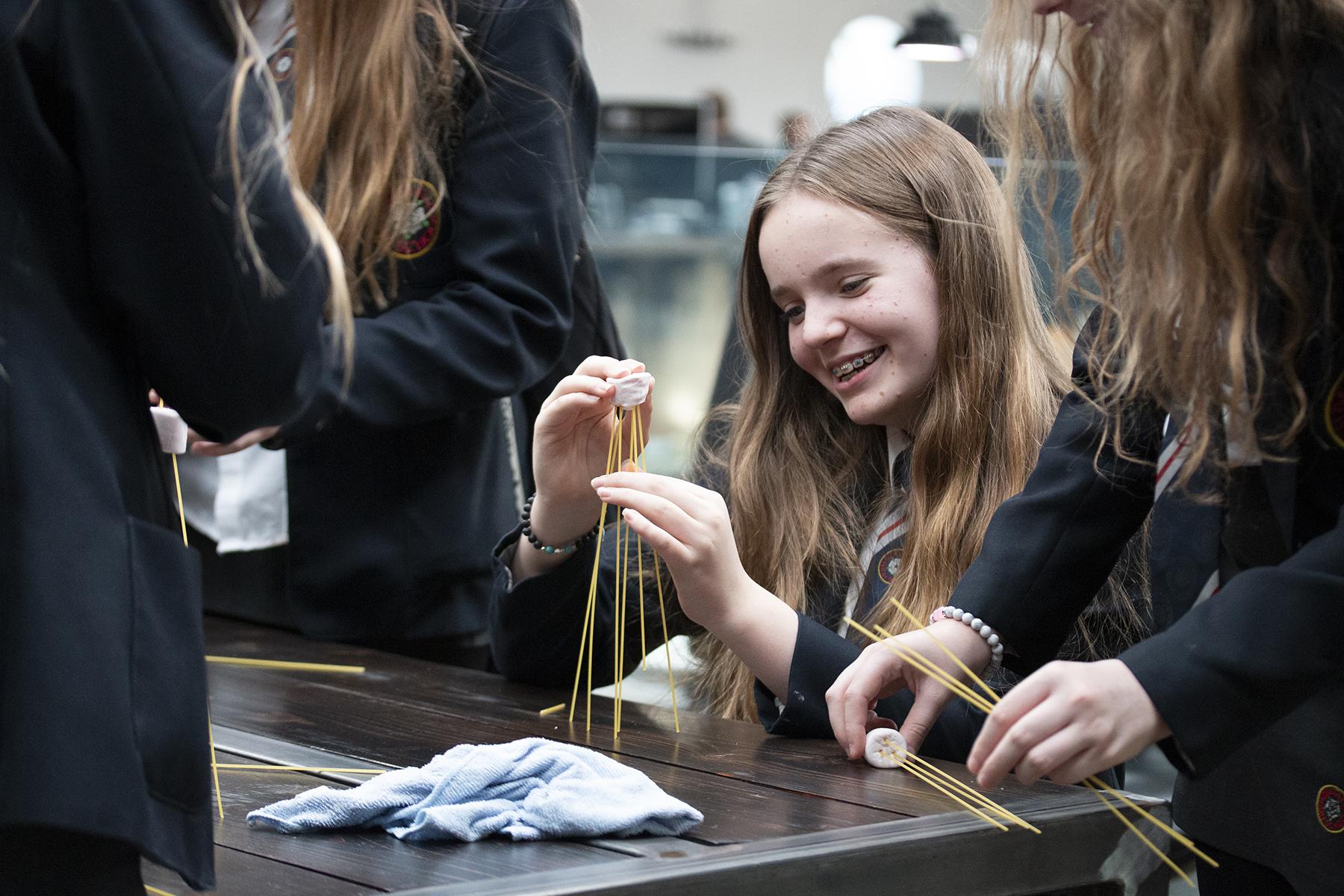 Female school students completing spaghetti and marshmallow tower challenge
