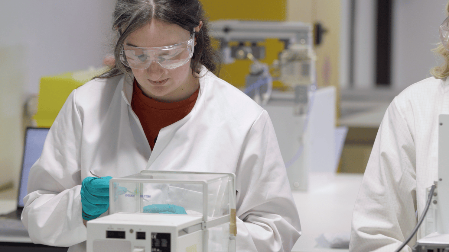 A woman with dark hair and eye protection weighing powders in a laboratory