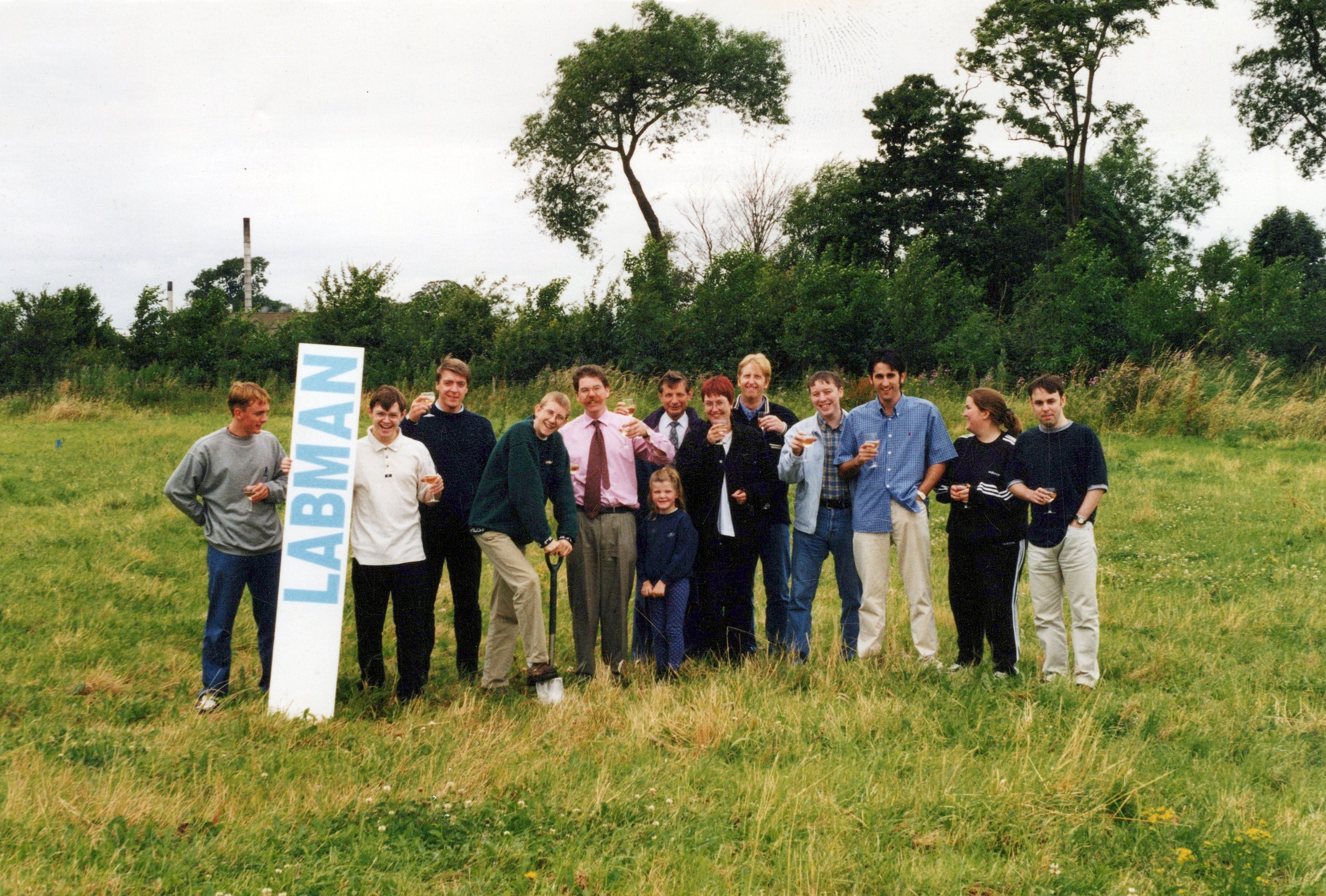 A group of people in a field holding a vertical Labman sign on an overcast day