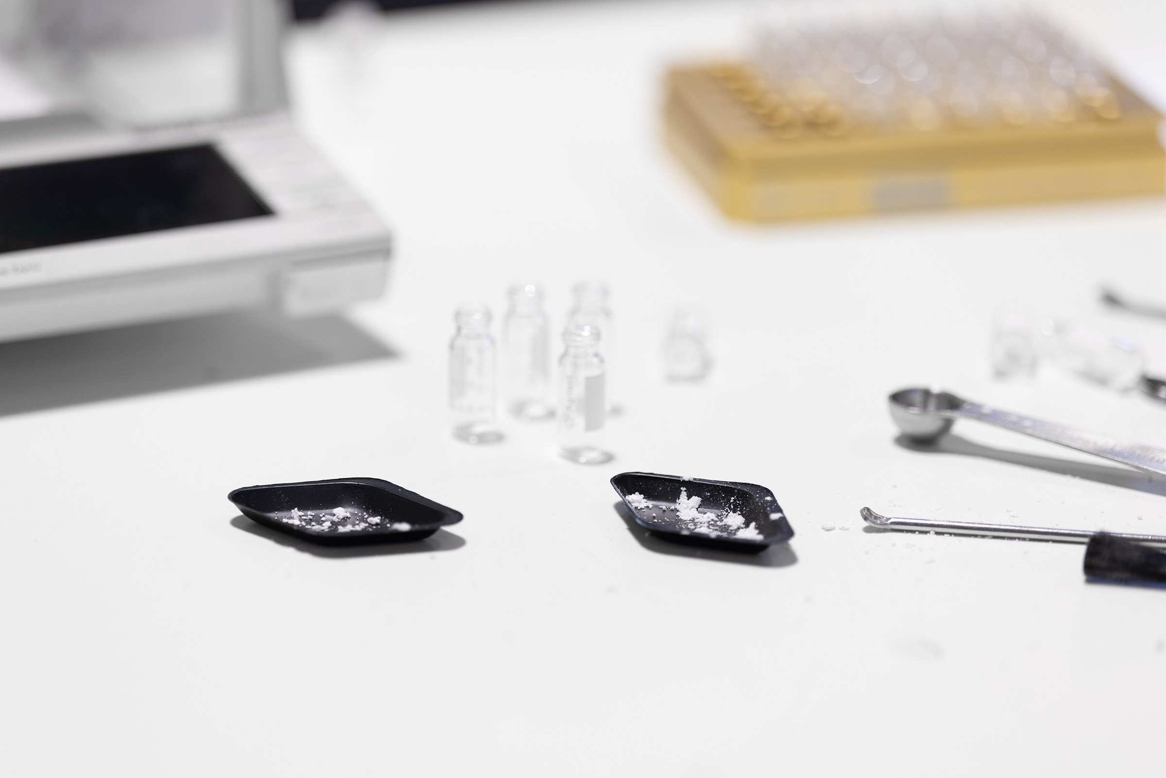Small trays of powder with spatulas, vials and a balance scattered on a table in the lab