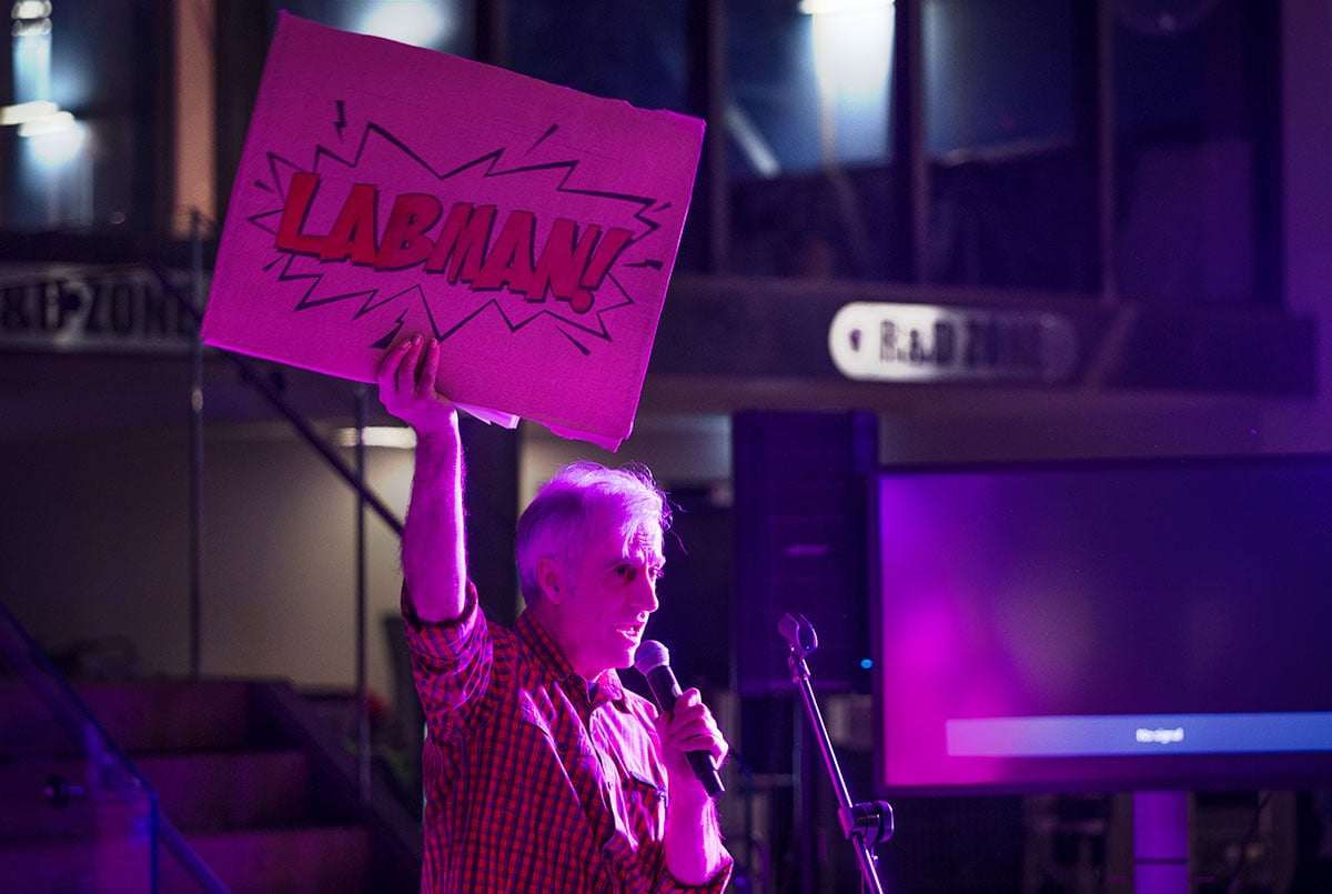Man wearing black and red checked shirt holding up sign saying "LABMAN!"