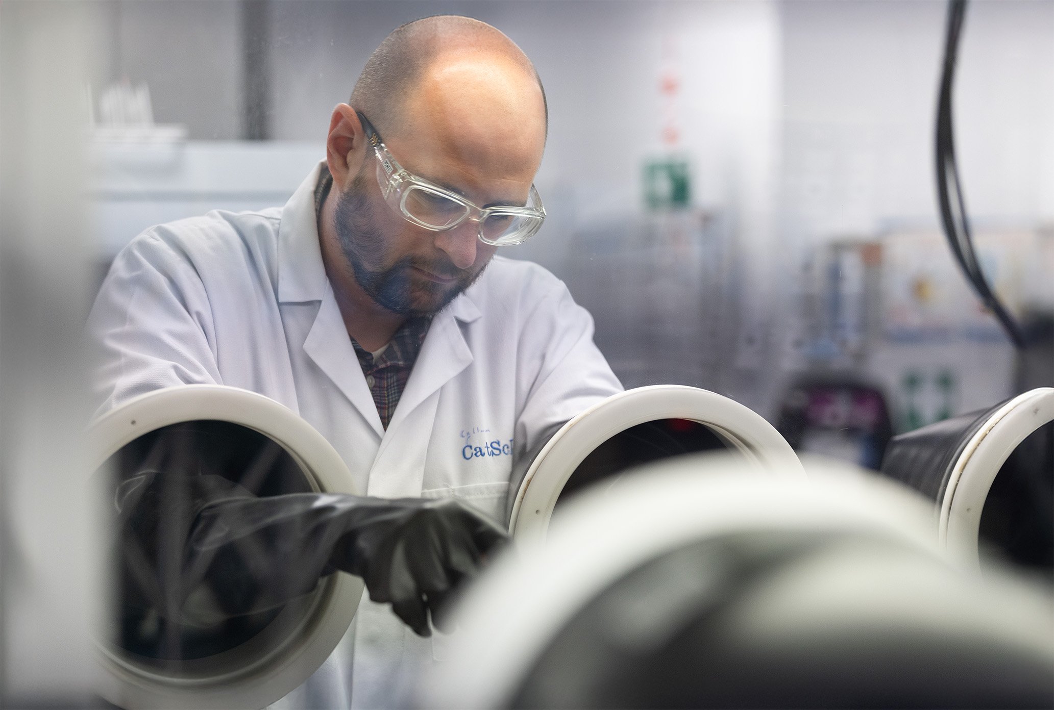 A man using a glovebox wearing safety specs in a laboratory