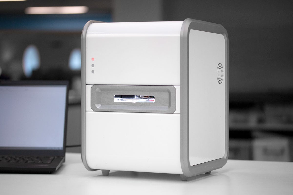 A white cuboid medical device with a grey laptop next to it in a lab