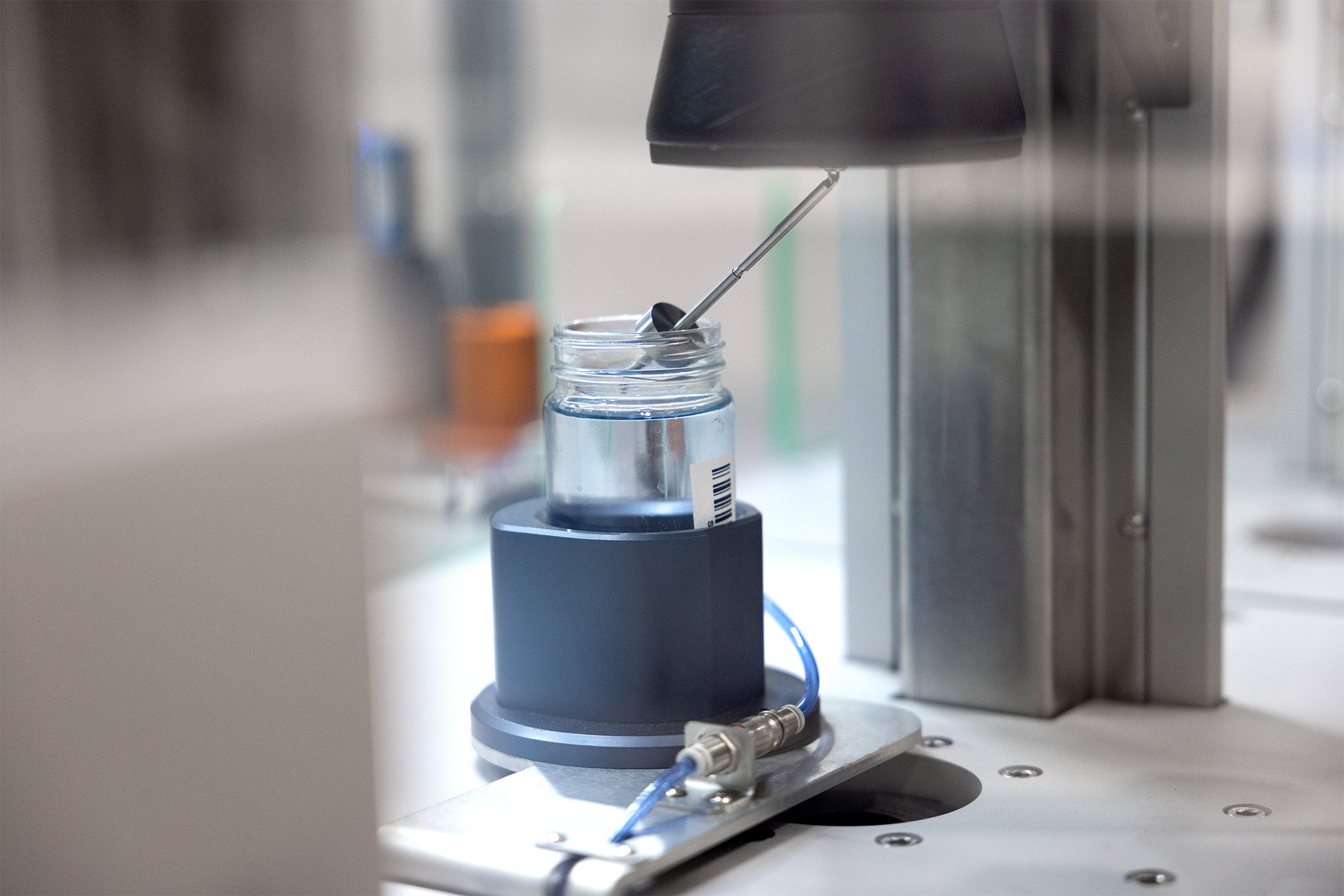 A geometry used for taking viscometry measurements being lowered into a jar of liquid on an angle
