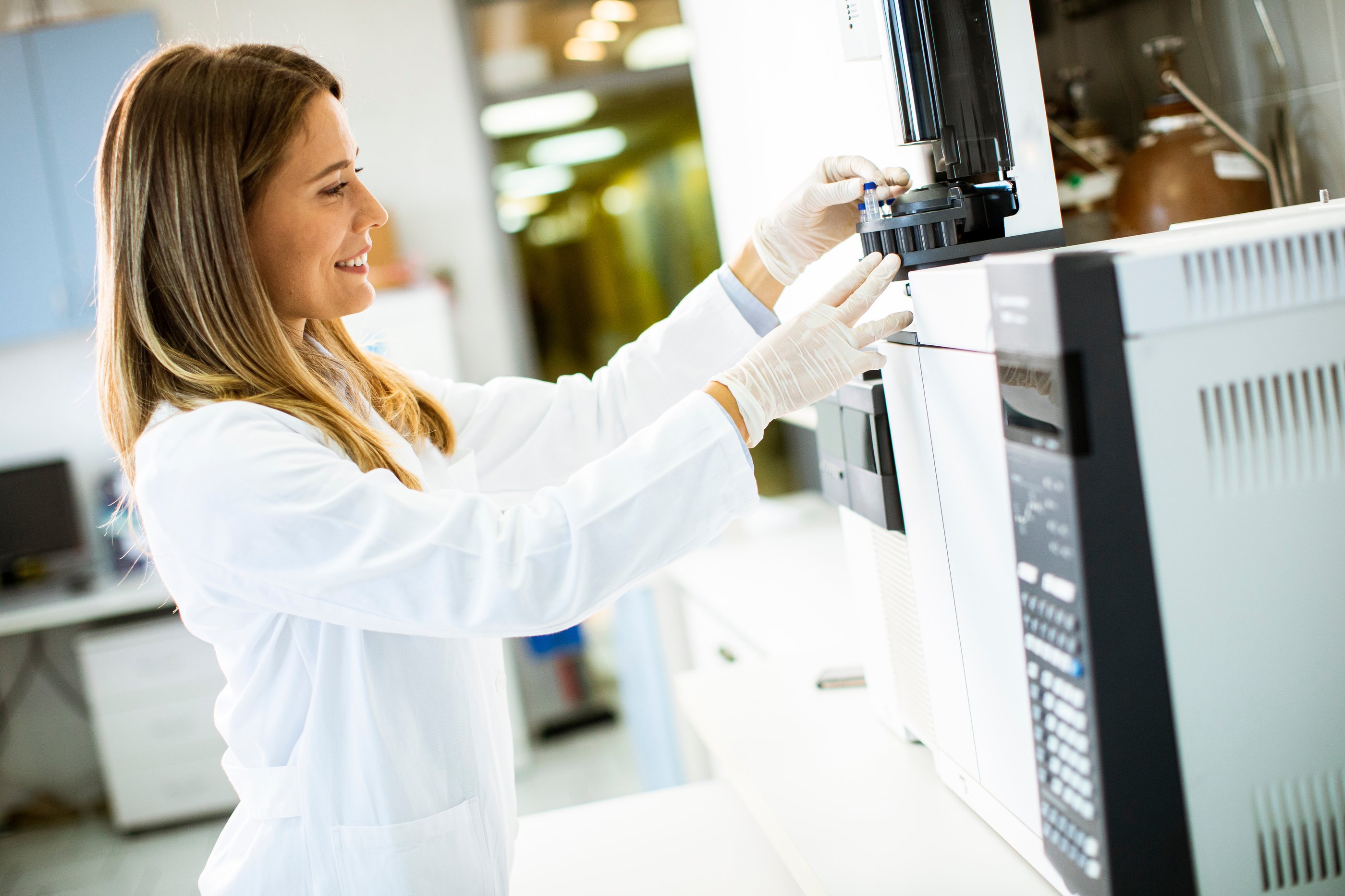 Smiling woman wearing white lab coat and white gloves is loading an automated purification system