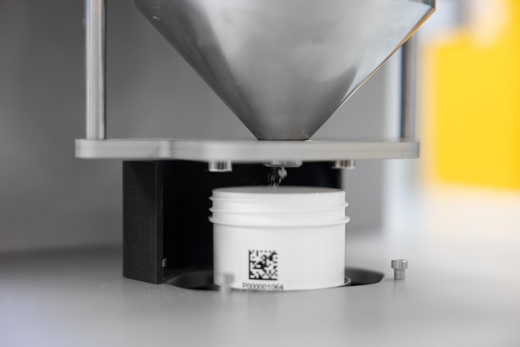 Close up of an automated system dispensing powder into a barcoded pot