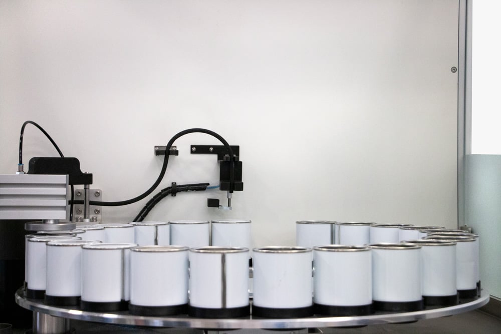 a ring of white paint tins with a robot above dispensing paint 
