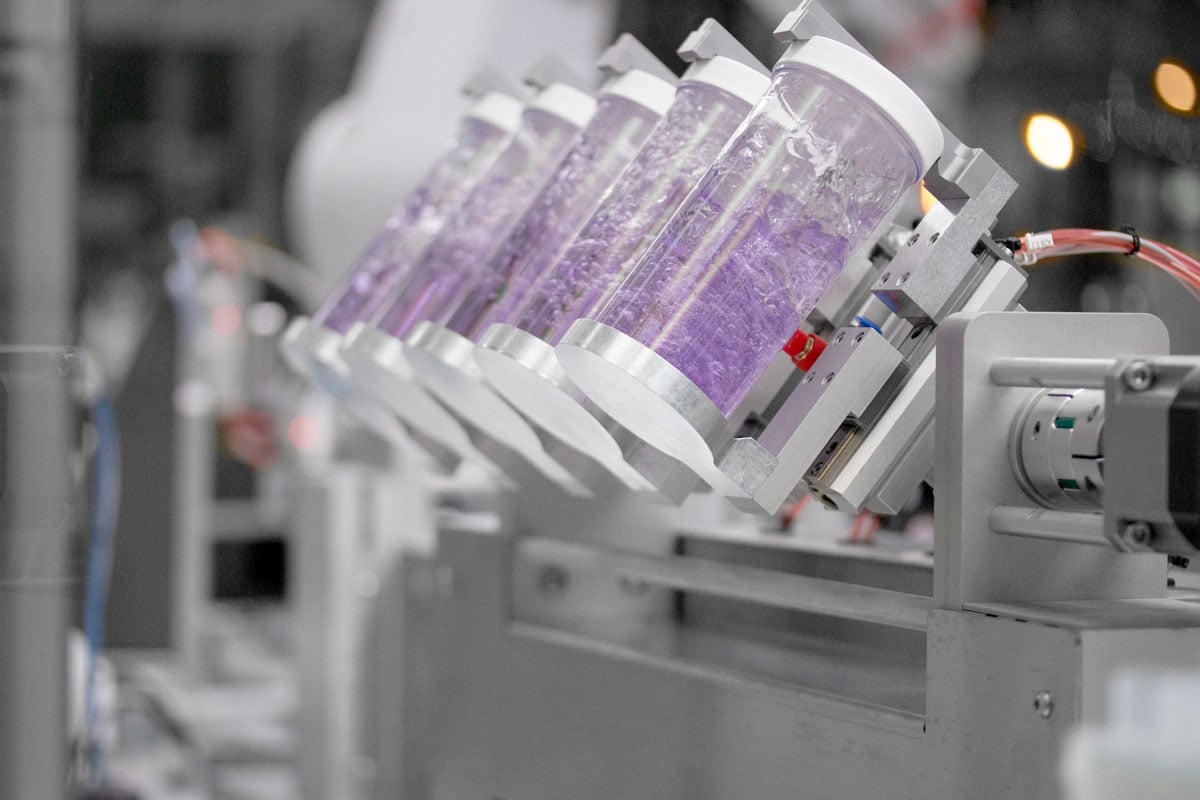 Multiple sample vials with purple liquid being shaken back and forth by a robotic formulation system