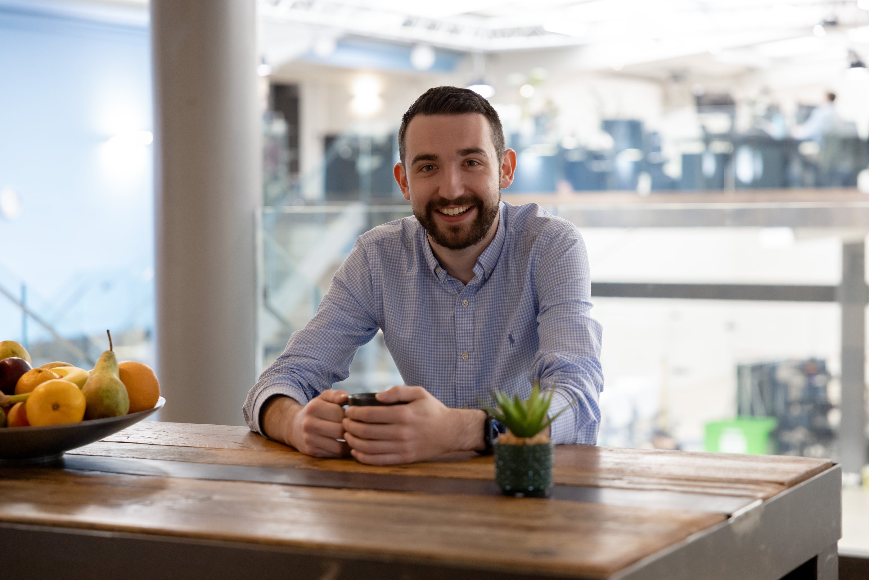 White man in a blue shirt with a short beard sitting at a table in an office 