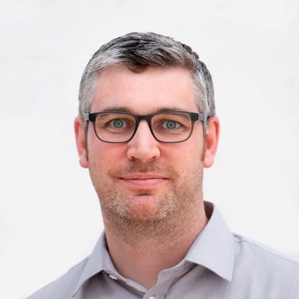 A headshot of a man with glasses smiling on a white background