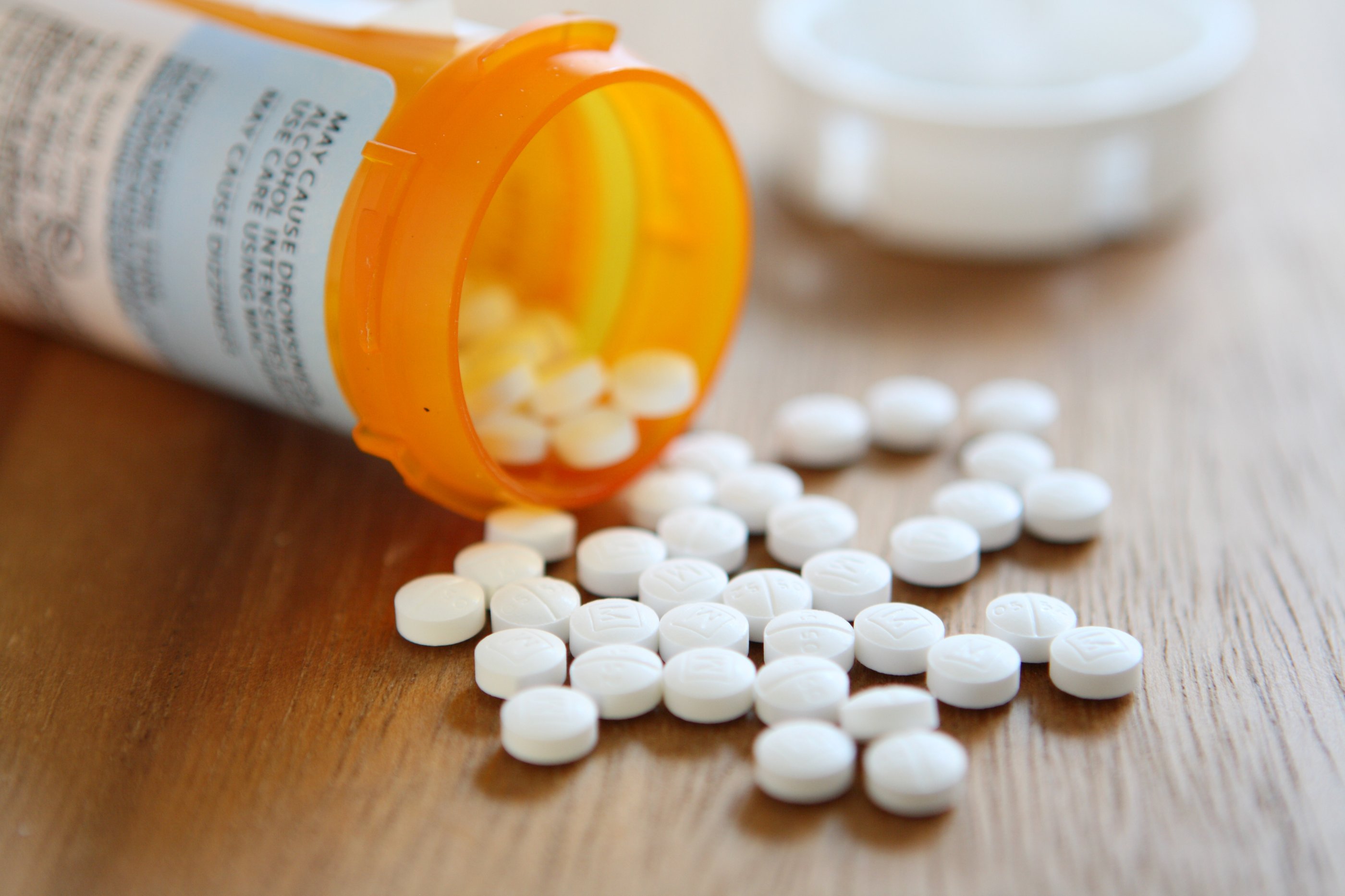 Orange pill pot is laid on its side on a wooden table, it has no lid on and the tablets have spilled out onto the table