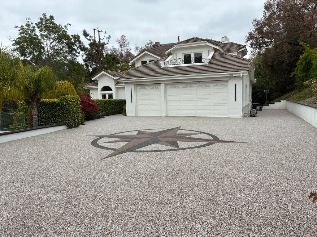 A beautiful home with a newly installed stone carpet driveway featuring a large, decorative compass rose inlay in the center. The driveway leads up to a two-car garage.