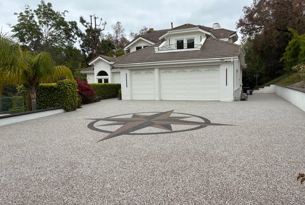 A beautiful home with a newly installed stone carpet driveway featuring a large, decorative compass rose inlay in the center. The driveway leads up to a two-car garage.
