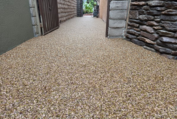 Stone carpet walkway with natural river pebbles and epoxy binder, creating a seamless, slip-resistant surface between residential walls.